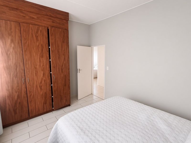 A clean bedroom featuring neutral walls, tiled flooring, and a large built-in wooden wardrobe providing ample storage space.