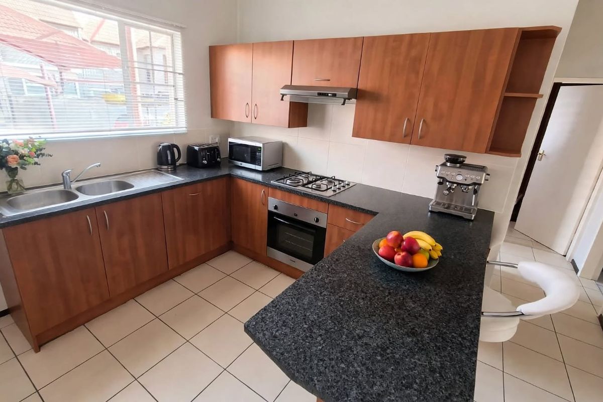 Functional kitchen featuring laminate cabinetry, granite countertops, gas hob, built-in oven, extractor fan, and tiled flooring.
