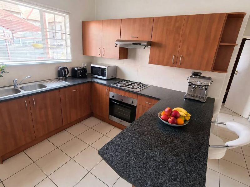 Functional kitchen featuring laminate cabinetry, granite countertops, gas hob, built-in oven, extractor fan, and tiled flooring.