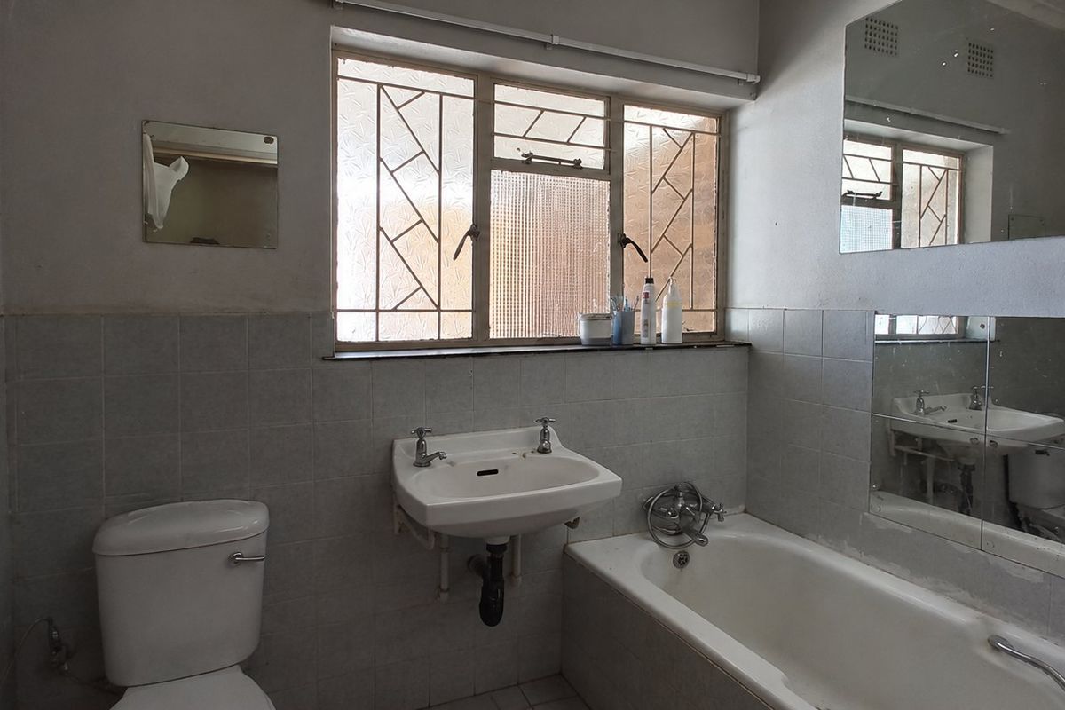 A dated bathroom featuring a pedestal washbasin, bathtub, and toilet with tiled walls and security bars on the window.