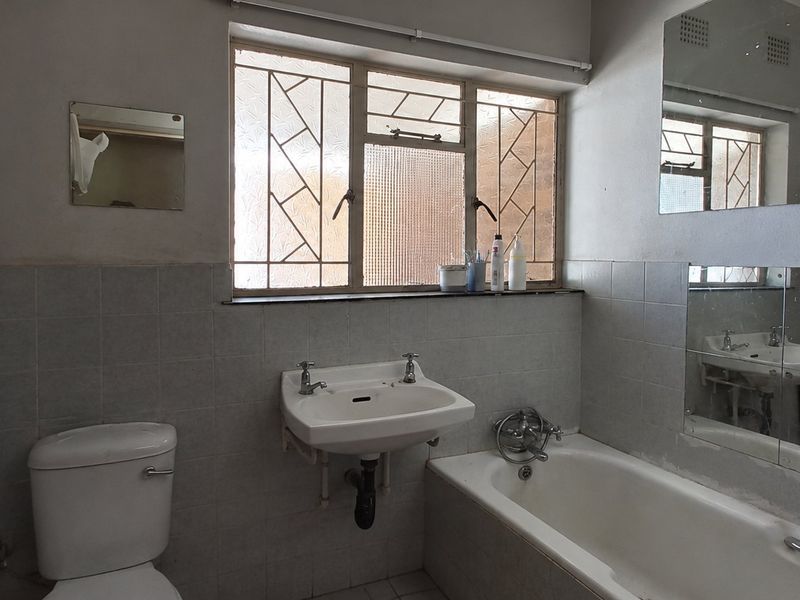 A dated bathroom featuring a pedestal washbasin, bathtub, and toilet with tiled walls and security bars on the window.