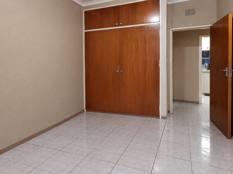 An empty bedroom featuring tiled flooring and built-in wooden cupboards, offering a neutral canvas for personalization.