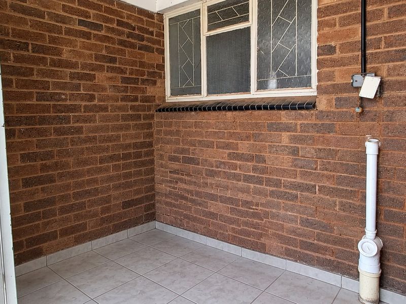 A functional outdoor utility or service area featuring exposed brick walls, tiled flooring, a security gate, and external plumbing connections.