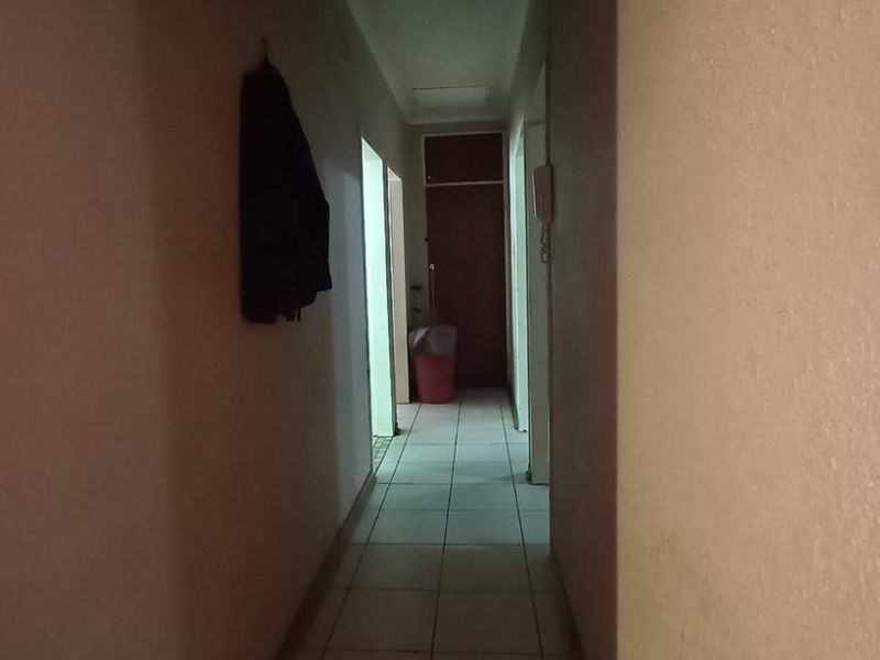 A narrow residential hallway featuring tiled flooring and access to multiple internal rooms, requiring minor cosmetic updates to improve the overall aesthetic.