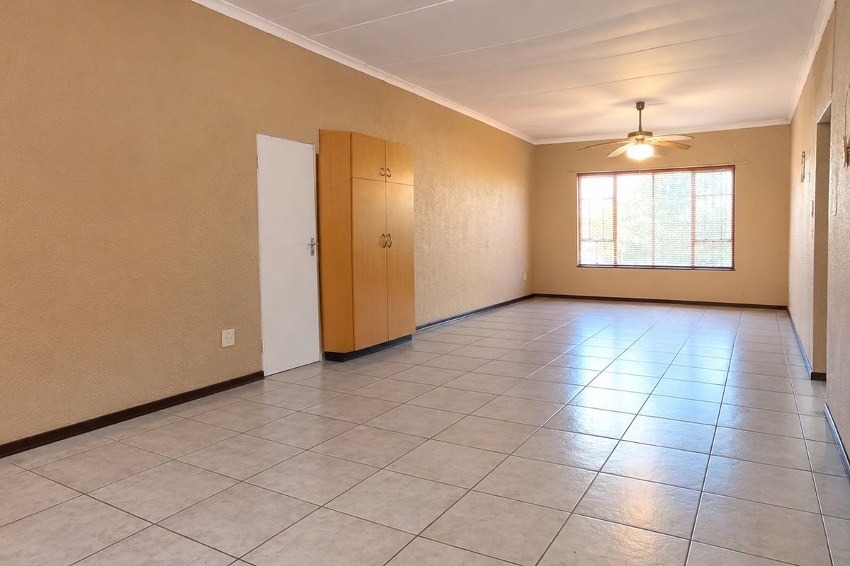 Spacious, empty living area featuring neutral tiled flooring, a ceiling fan, and a built-in storage cupboard, offering a blank canvas for personalization.