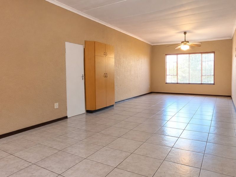 Spacious, empty living area featuring neutral tiled flooring, a ceiling fan, and a built-in storage cupboard, offering a blank canvas for personalization.