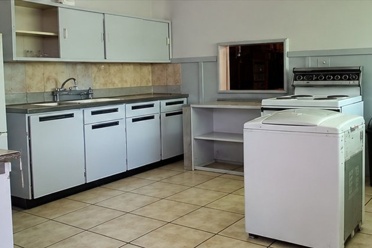 A dated kitchen featuring original cabinetry, tiled backsplash, and a functional layout with a pass-through window, offering potential for modern renovation.