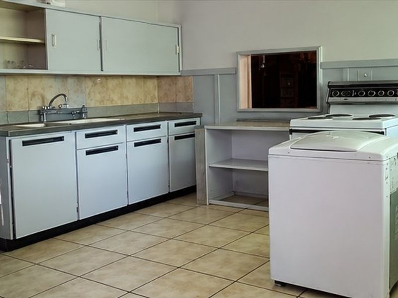A dated kitchen featuring original cabinetry, tiled backsplash, and a functional layout with a pass-through window, offering potential for modern renovation.