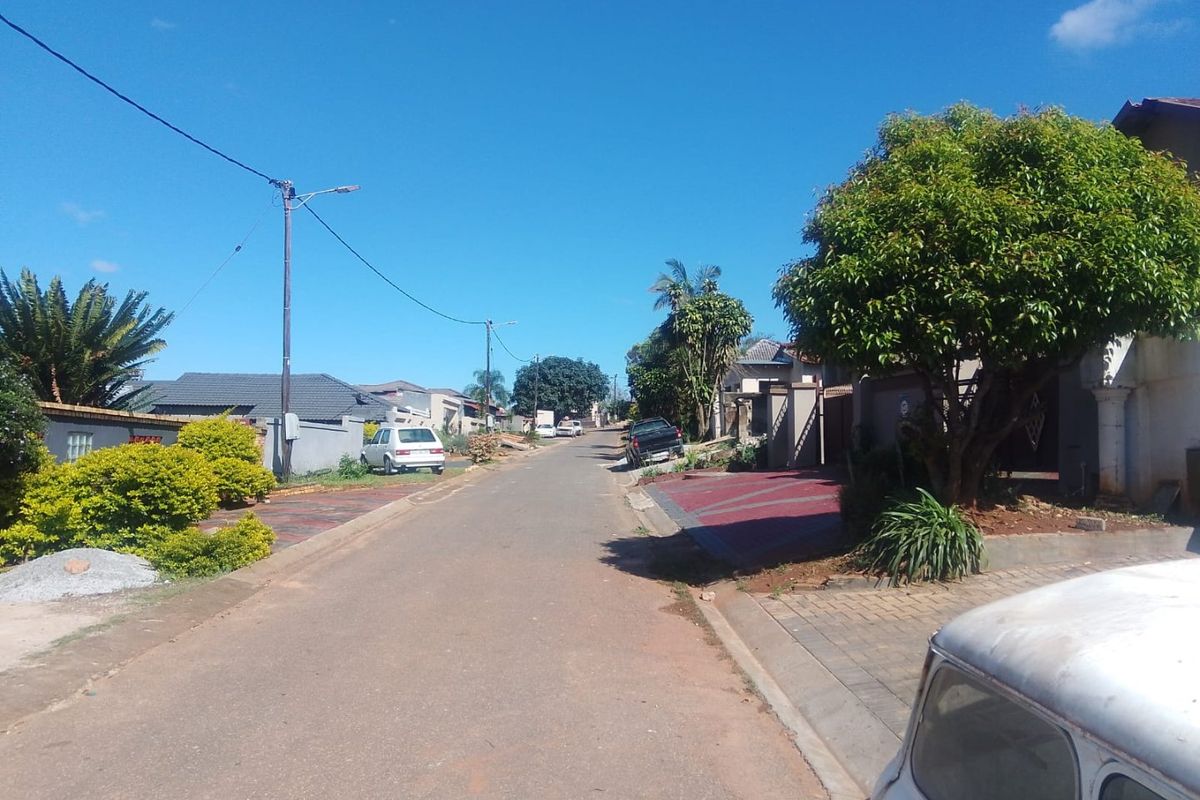 A view of the residential street showing the neighborhood approach, paved driveways, and boundary walls of the surrounding properties.