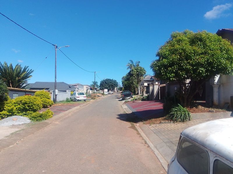 A view of the residential street showing the neighborhood approach, paved driveways, and boundary walls of the surrounding properties.