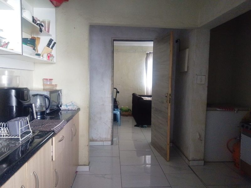 A functional kitchen area featuring built-in cabinetry, granite countertops, and tiled flooring, leading through to an adjacent room.