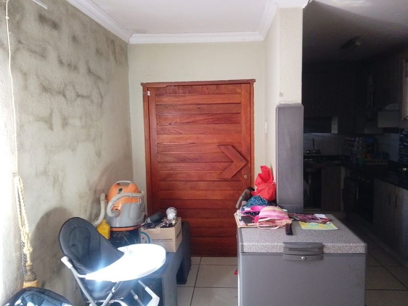 A utility or scullery area featuring tiled flooring and a solid wooden door, requiring wall surface repairs and cosmetic updates.