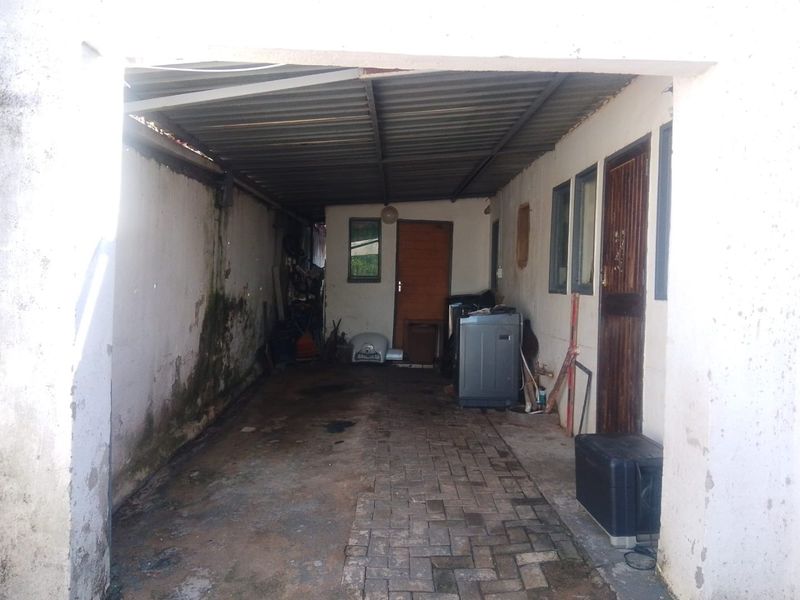 A covered outdoor garage or utility area featuring paved flooring, corrugated roofing, and direct access to the main building structure.