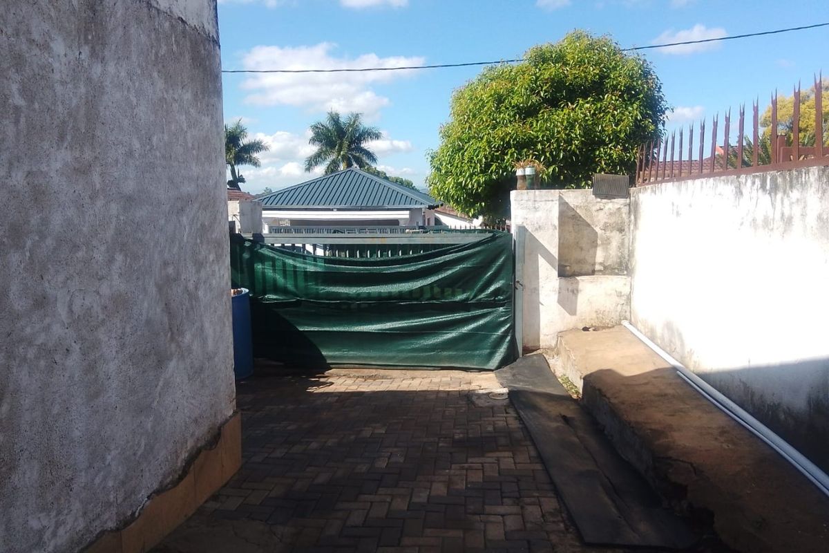 A rear exterior area featuring a paved driveway, perimeter wall with security spikes, and a gated entrance.