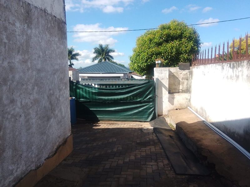 A rear exterior area featuring a paved driveway, perimeter wall with security spikes, and a gated entrance.