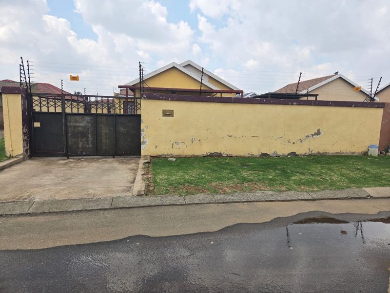 Front view of the property featuring a perimeter wall with electric fencing, a sliding metal gate, and a concrete driveway.