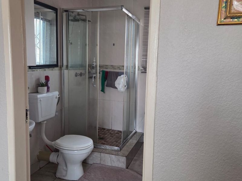 A functional bathroom featuring a corner shower enclosure, toilet, and tiled finishes throughout.