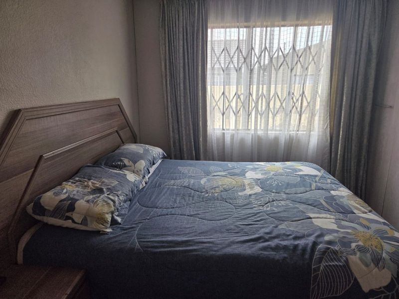 A functional bedroom featuring a window with a fitted security gate and curtains.