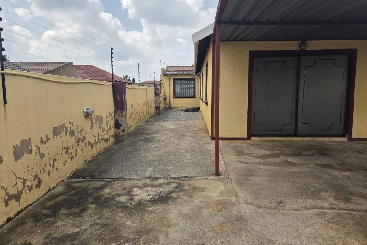 Rear exterior view showing a concrete driveway, covered patio area, and perimeter wall with electric fencing.