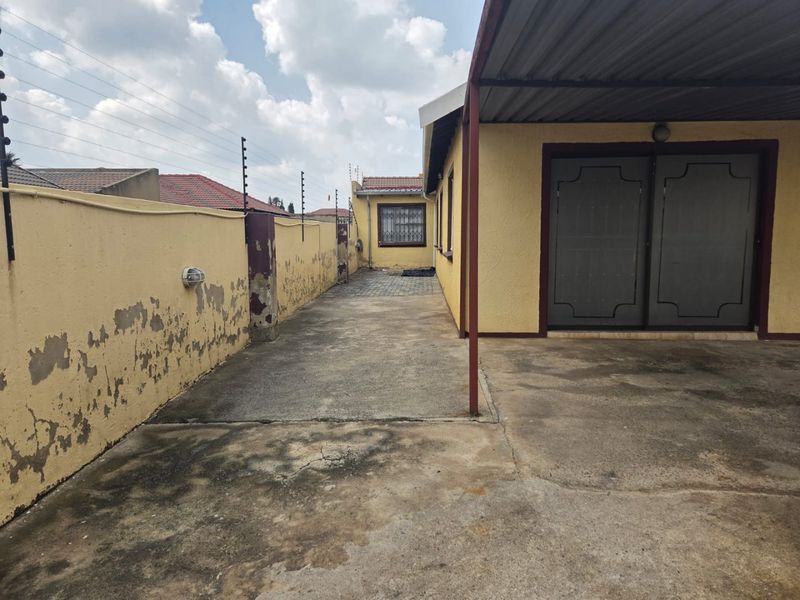 Rear exterior view showing a concrete driveway, covered patio area, and perimeter wall with electric fencing.