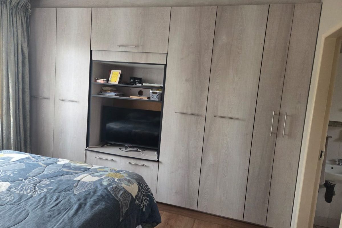 A bedroom featuring extensive light wood-grain built-in cupboards with integrated shelving and storage, complemented by durable laminate flooring.