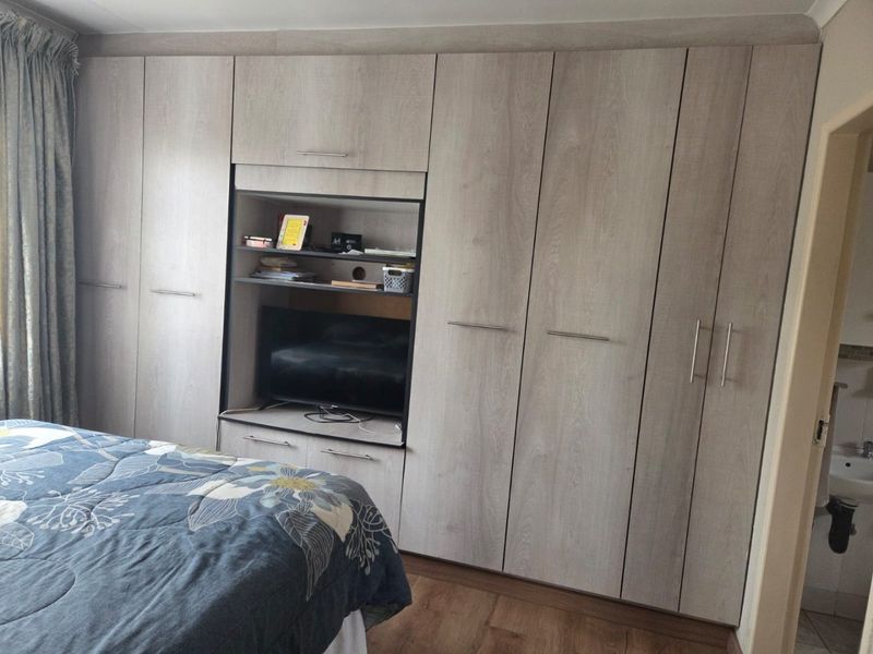 A bedroom featuring extensive light wood-grain built-in cupboards with integrated shelving and storage, complemented by durable laminate flooring.
