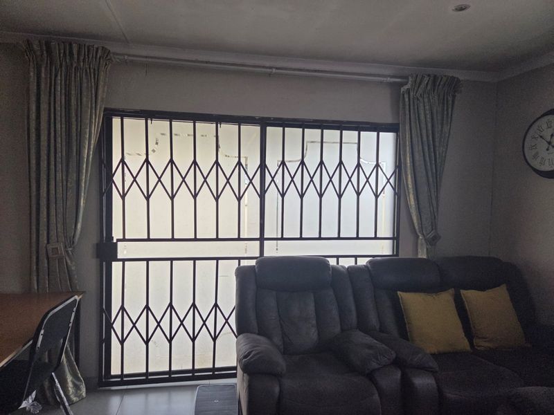 A living room area featuring tiled flooring, recessed ceiling lighting, and a sliding security gate providing access to the exterior.
