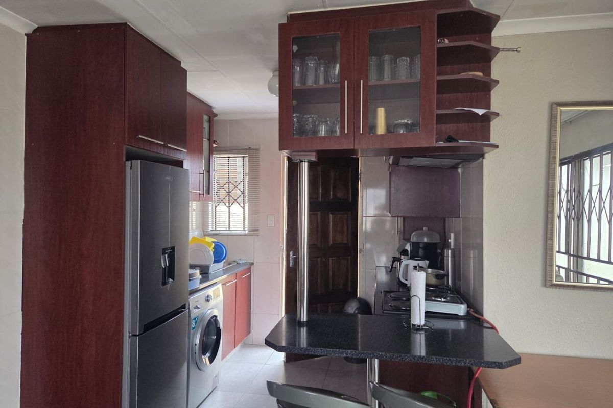 Compact kitchen featuring dark wood-look cabinetry, a breakfast bar, tiled backsplash, and integrated space for laundry appliances.