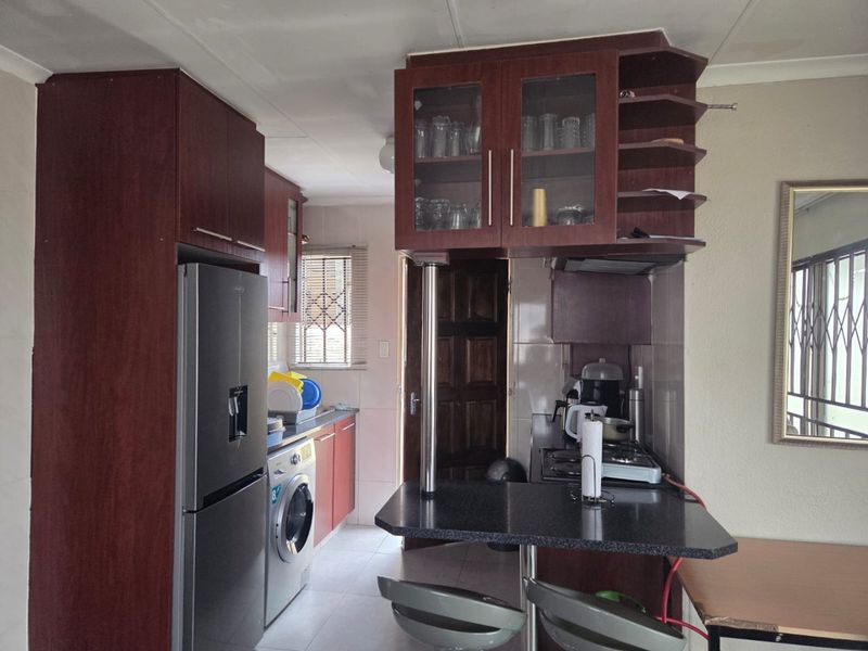 Compact kitchen featuring dark wood-look cabinetry, a breakfast bar, tiled backsplash, and integrated space for laundry appliances.