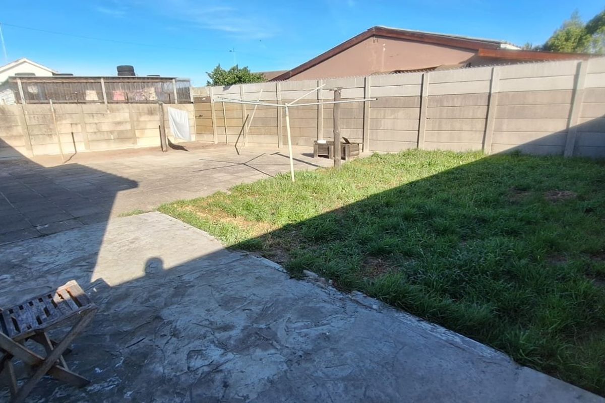 A rear garden featuring a paved patio area, a section of lawn, and a precast concrete boundary wall.