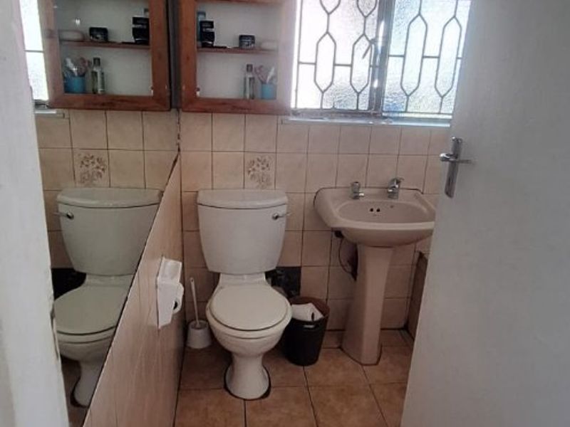 A compact bathroom featuring a pedestal basin, toilet, tiled walls and flooring, and a large wall mirror with security bars on the window.