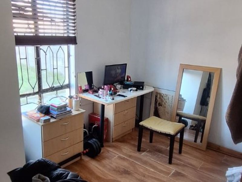 A bedroom featuring wood-look tile flooring, burglar bars, and venetian blinds, currently showing signs of ceiling water damage and paint deterioration.