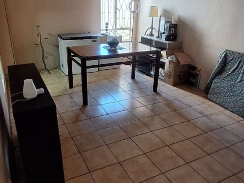 A living area featuring tiled flooring, a timber-clad ceiling with a fan, and a window fitted with a security gate.