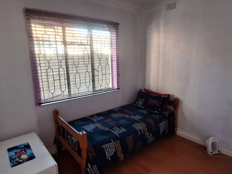 A compact bedroom featuring laminate flooring, a window with security bars, and venetian blinds. The room requires cosmetic updates to the wall finishes.