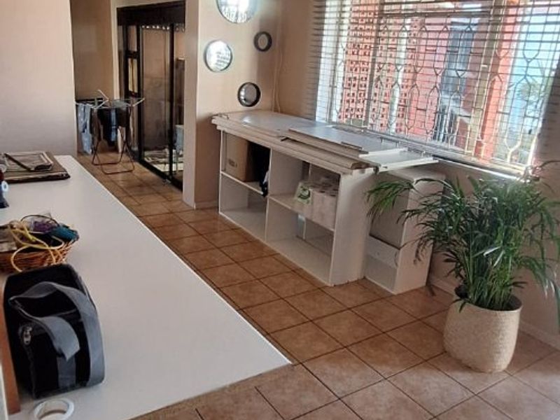 A functional utility or workspace area featuring tiled flooring, a ceiling fan, and security bars on the windows.