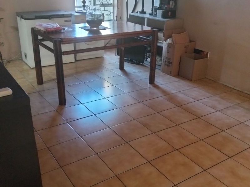 A living area featuring ceramic floor tiles and a window with a security gate, requiring cosmetic updates to improve the overall aesthetic.