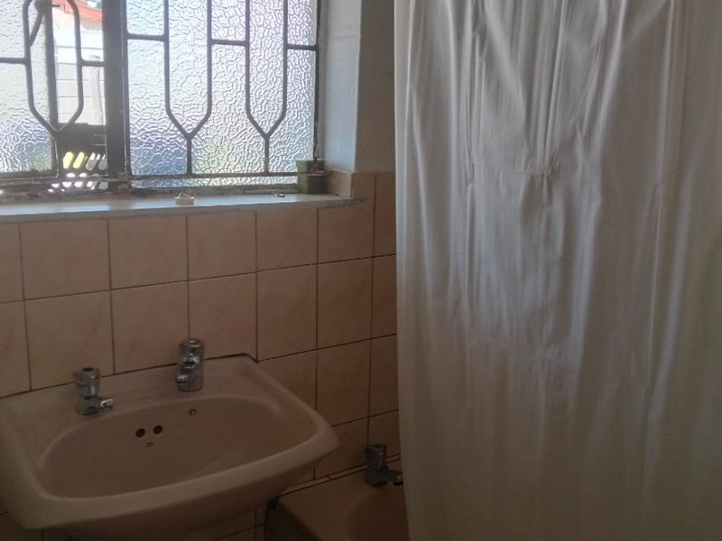 A functional bathroom featuring a pedestal basin, bathtub with shower curtain, and tiled finishes, requiring some maintenance and cosmetic updates.