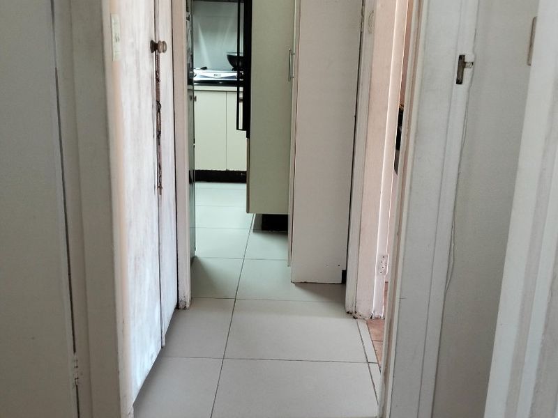 A narrow hallway with tiled flooring and built-in storage cupboards, providing access to adjacent rooms including a kitchen area.