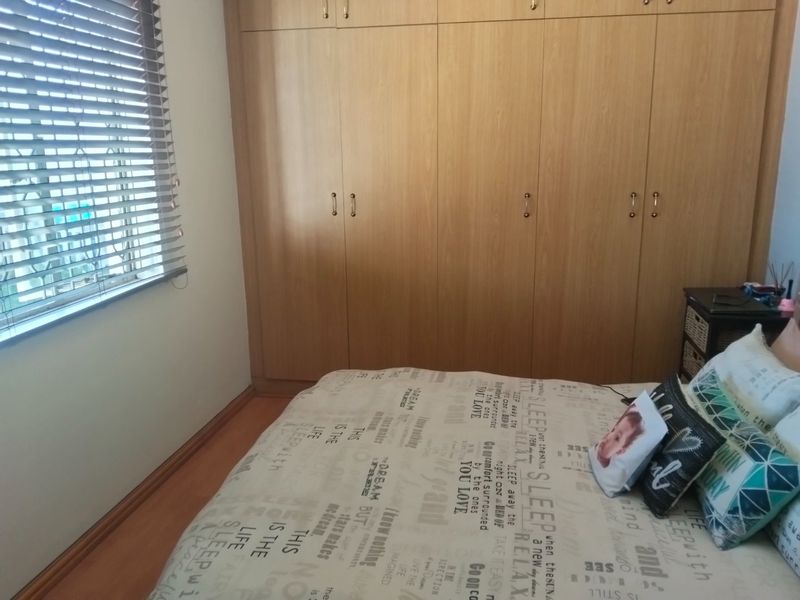 A well-maintained bedroom featuring extensive floor-to-ceiling built-in wooden cupboards, laminate flooring, and venetian blinds for light control.
