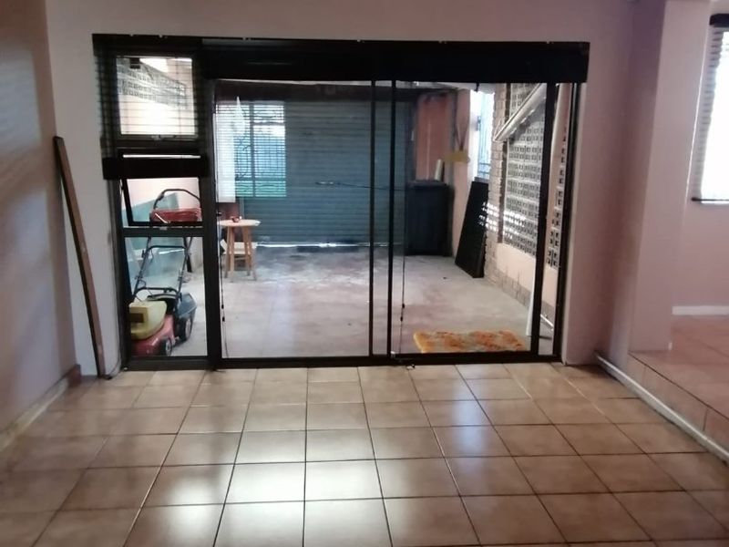 An empty living room featuring tiled flooring and a sliding glass door leading to an outdoor area, with a timber ceiling finish.