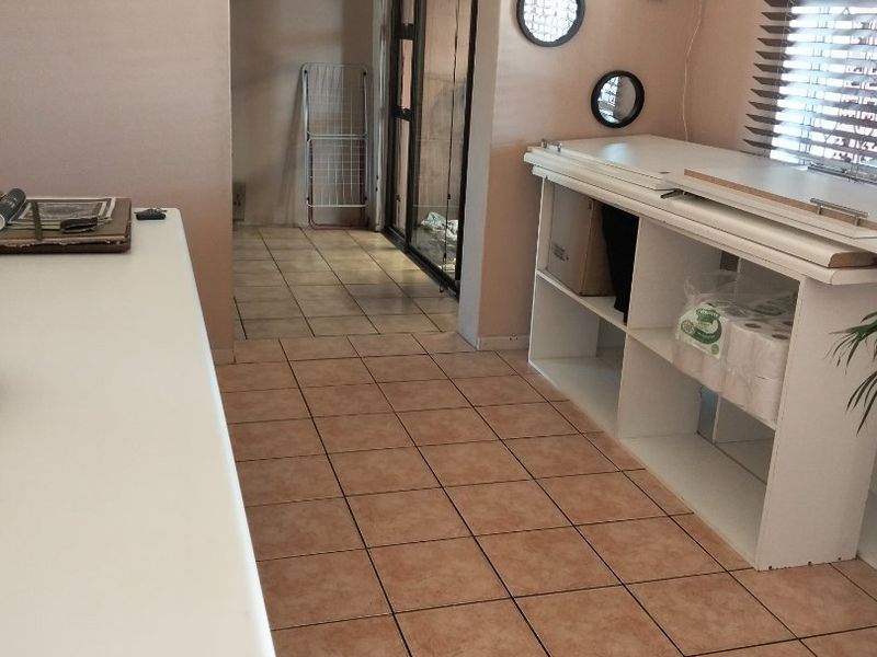 A functional laundry or utility space featuring tiled flooring, venetian blinds, and direct access to an adjacent area through a sliding glass door.