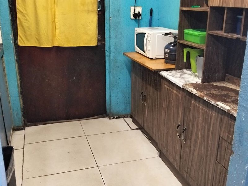 A compact kitchen area featuring built-in wooden cabinetry, laminate countertops, and tiled flooring, requiring cosmetic updates to improve the overall aesthetic.