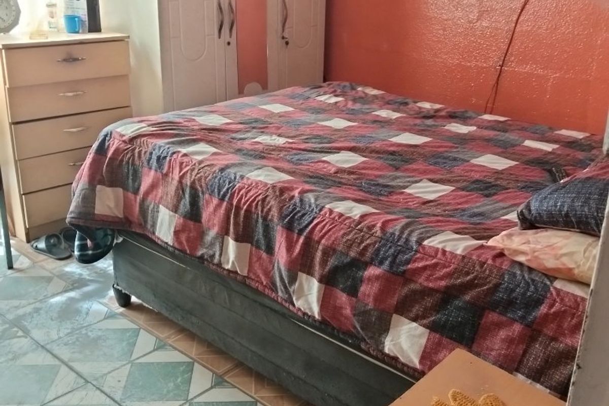 A bedroom featuring tiled flooring and a built-in wardrobe, currently showing signs of wear and dated finishes.