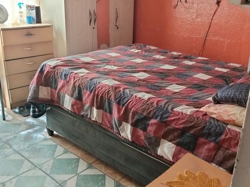 A bedroom featuring tiled flooring and a built-in wardrobe, currently showing signs of wear and dated finishes.