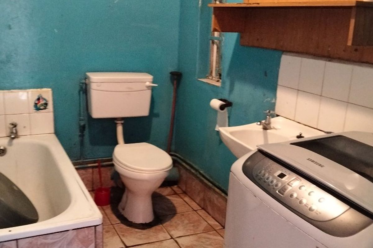 A functional bathroom featuring a bathtub, toilet, and wall-mounted basin with tiled finishes, currently showing signs of age and wear.
