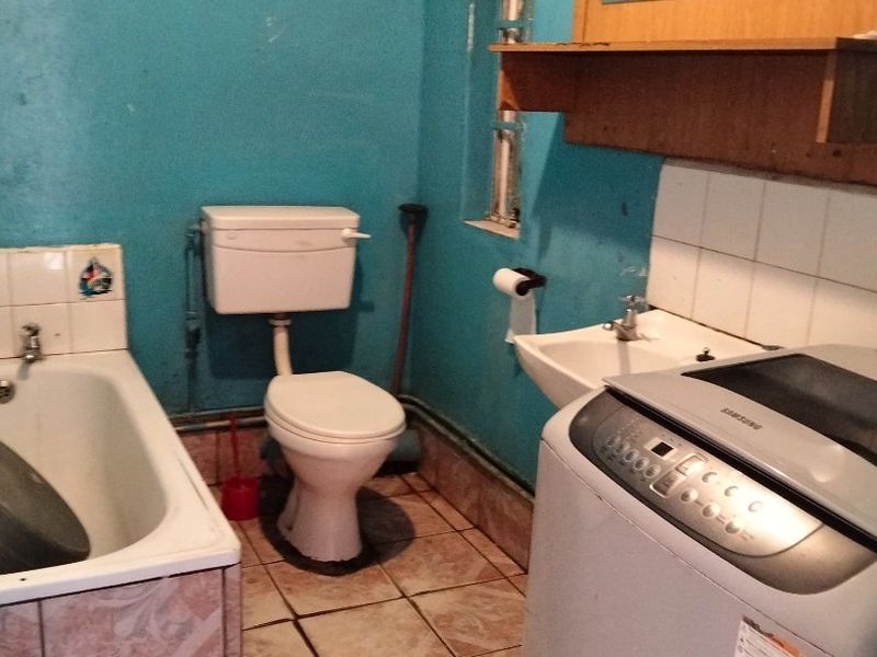 A functional bathroom featuring a bathtub, toilet, and wall-mounted basin with tiled finishes, currently showing signs of age and wear.