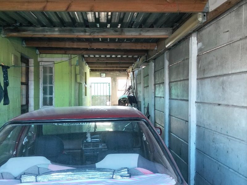 A covered carport or garage area featuring exposed timber rafters, corrugated metal roofing, and precast concrete wall panels.