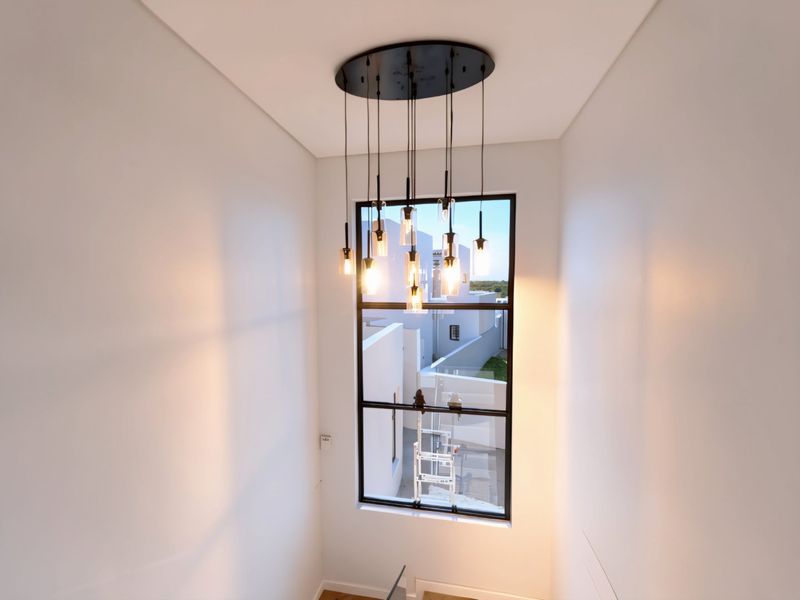 A bright, modern hallway featuring a large black-framed window and a contemporary multi-pendant light fixture, offering a clean and minimalist aesthetic.