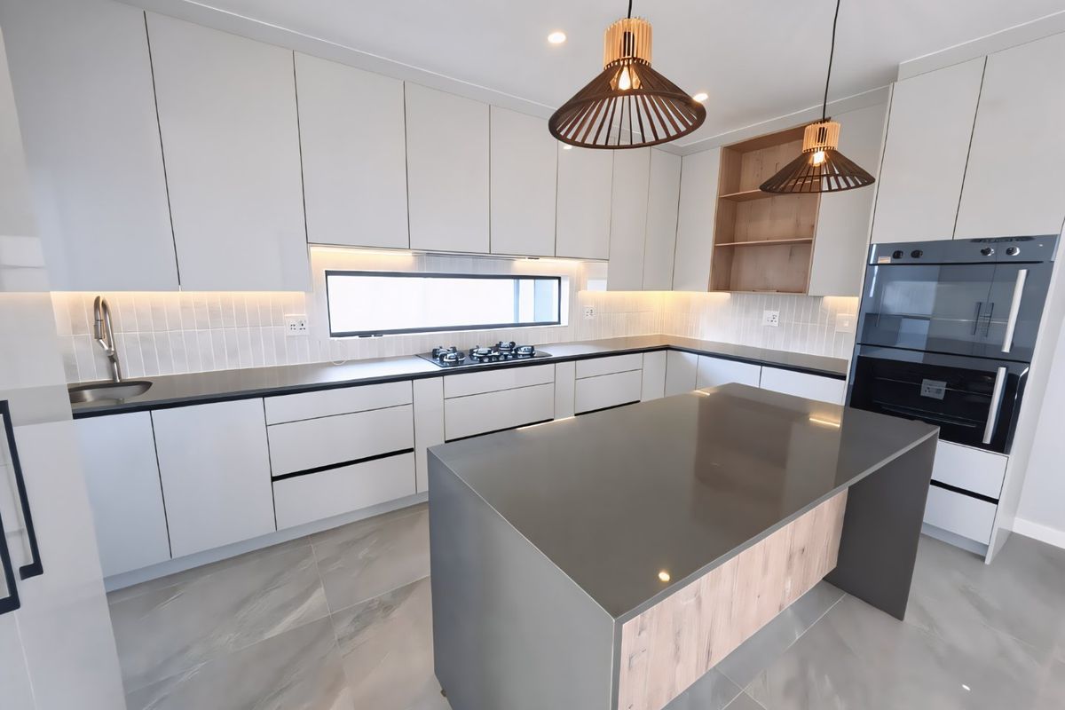 Modern kitchen featuring sleek white cabinetry, stone countertops, a central island, built-in double oven, gas hob, and contemporary tiled backsplash with integrated lighting.