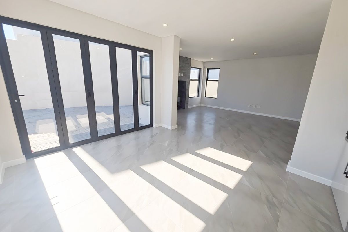 Spacious, light-filled living area featuring large format floor tiles, modern recessed lighting, a stone-clad fireplace, and expansive aluminium stacker doors leading to the exterior.